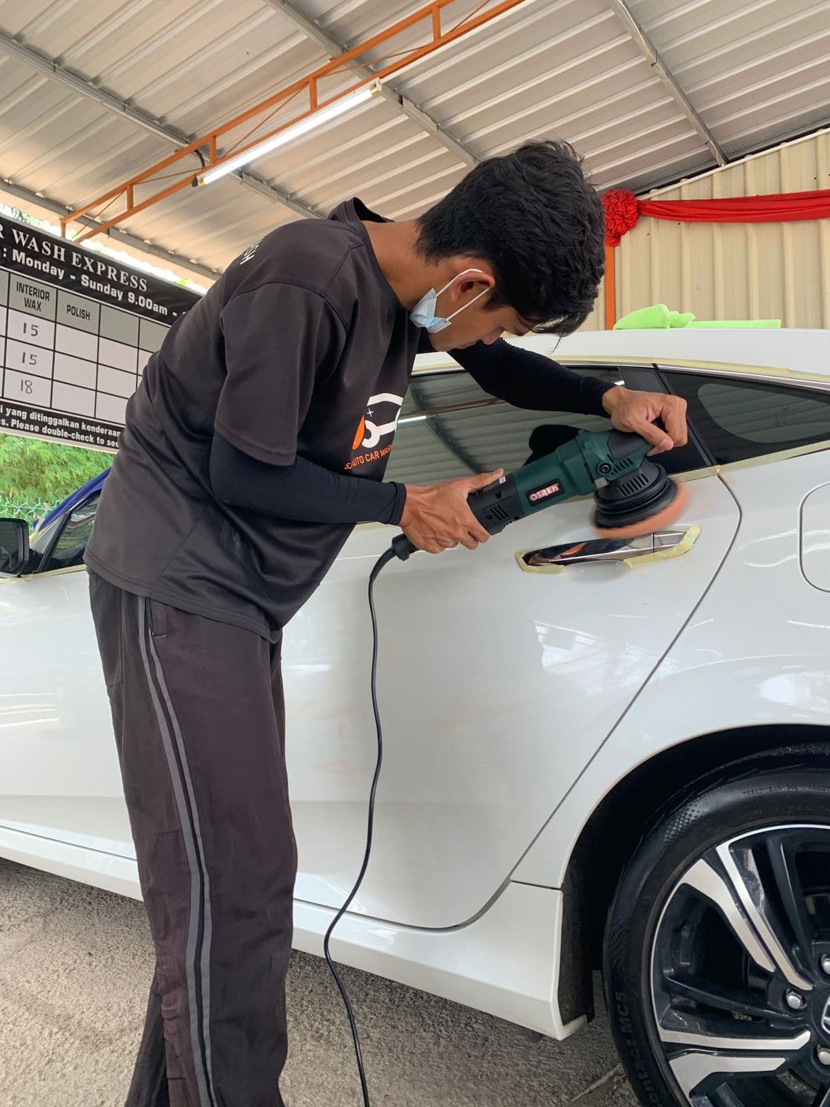 A staff member machine-polishing a white car at SJ Auto Car Wash
